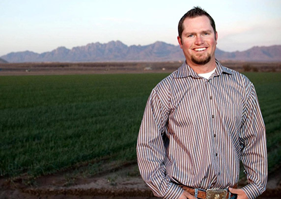 Jay Hill stands in front of a green field in front of a mountain range.