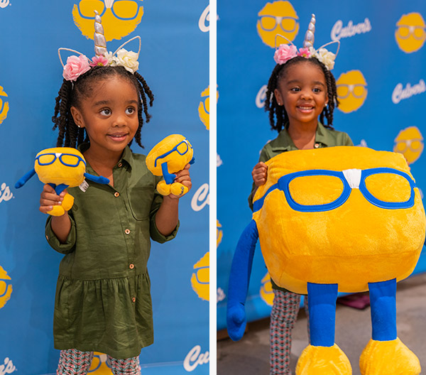 A young girl holds up Curdis plushes and smiles for a photo in front of a Culver’s backdrop